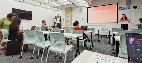 Instructor at podium presents to students in a modern classroom with a large screen.